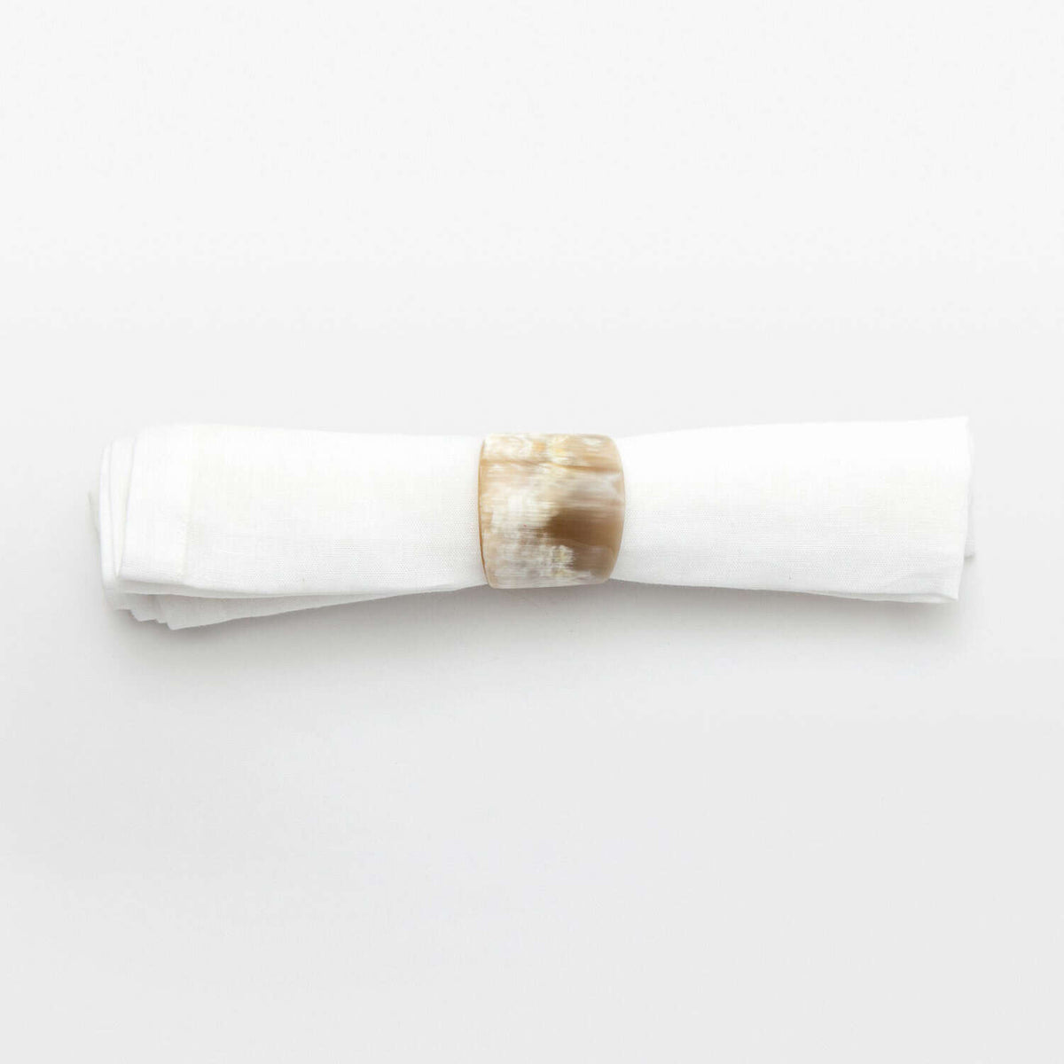 A white cloth napkin is neatly rolled and secured with a round, glossy James Natural Horn Napkin Ring by Blue Pheasant, set against a plain white background.