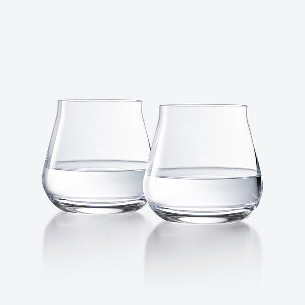 Two Chateau Barware glasses by Baccarat, half-filled with water, stand side by side on a reflective white surface with a light gray background.
