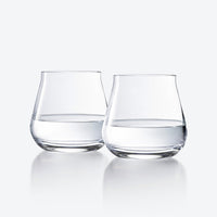 Two Chateau Barware glasses by Baccarat, half-filled with water, stand side by side on a reflective white surface with a light gray background.