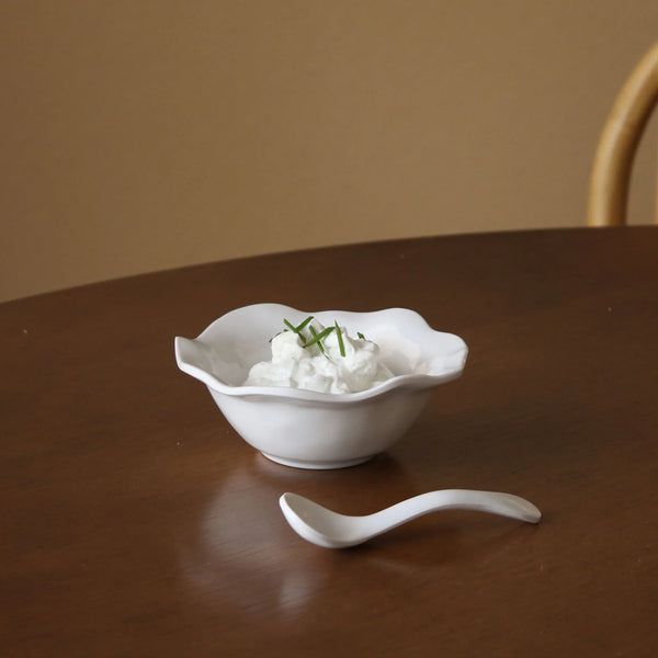 A small white bowl topped with whipped cream and chives sits on a wooden table beside a stylish, BPA-free Beatriz Ball Vida Havana Spoon - Mini, made of dishwasher-safe melamine.