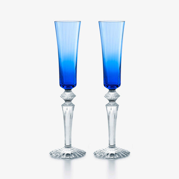 A pair of Baccarat Mille Nuits Flutissimo blue champagne flutes, featuring intricate faceted clear stems that evoke the elegance of crystal, are arranged side by side against a plain white background.