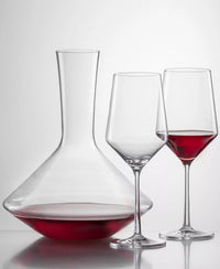A Zwiesel Pure Red Wine Decanter filled with red wine, standing next to an empty wine glass and a glass partially filled with red wine.
