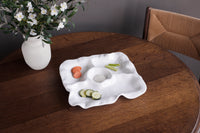 The Beatriz Ball Vida Havana Multi Chip & Dip platter, topped with veggies and dip, rests on a round wooden table beside a white flower vase and woven chair—an ideal choice for stylish outdoor entertaining.