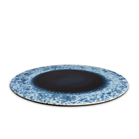 The Terra Platter Charger Indigo by L'Objet features a dark blue center and speckled blue and white rim, perfect for an elegant table setting when paired with porcelain placemats.