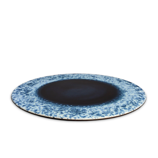 The Terra Platter Charger Indigo by L'Objet features a dark blue center and speckled blue and white rim, perfect for an elegant table setting when paired with porcelain placemats.