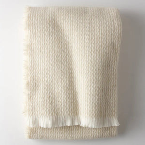 The Four Sided Pinstripe Fringe Throw by A Soft Idea, a folded cream wool blend with subtle fringe, adds a cozy blanket touch to any space.