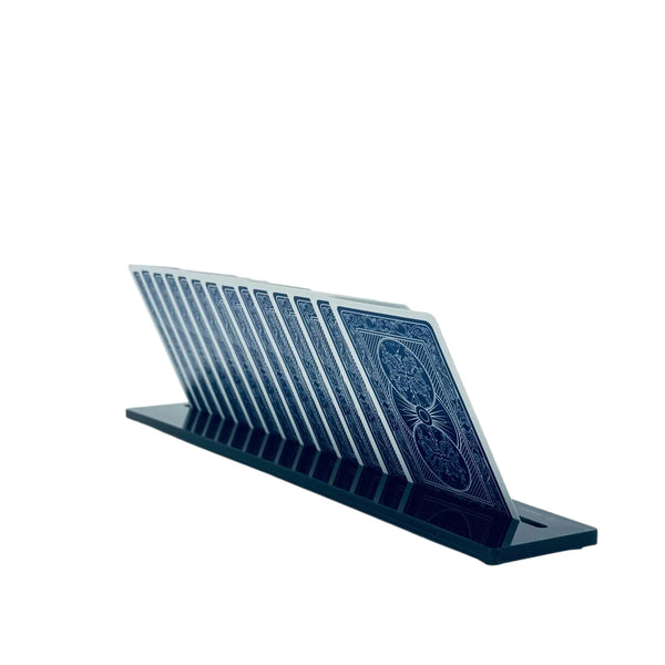 A row of playing cards with blue backs stands upright in a sleek black Luxe Dominoes Luxe Canasta & More Card Rack, set against a white background.
