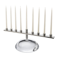 A Riverstone Simon Pearce Menorah featuring handmade glass with a long metal bar holding nine white taper candles.