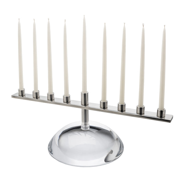 A Riverstone Simon Pearce Menorah featuring handmade glass with a long metal bar holding nine white taper candles.