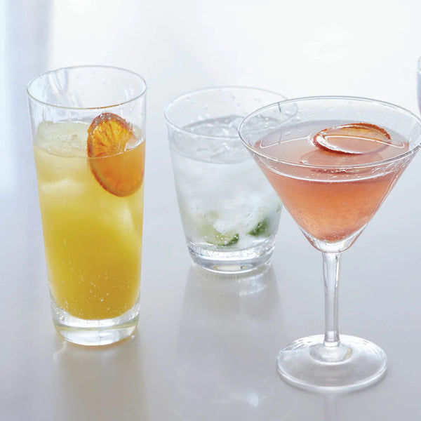 Three cocktails in elegant Mariposa Bellini Glassware: a yellow drink with orange slice in a tall glass, a clear drink with mint in a stemless wine glass, and a pink drink with orange slice in a martini glass.