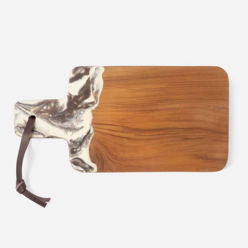 The Austin Swirled Cheeseboard by Blue Pheasant is a rectangular teak board with a handle, marbled white and gray resin accent near the handle, and a brown leather strap looped through a hole at the end.