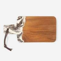 The Austin Swirled Cheeseboard by Blue Pheasant is a rectangular teak board with a handle, marbled white and gray resin accent near the handle, and a brown leather strap looped through a hole at the end.
