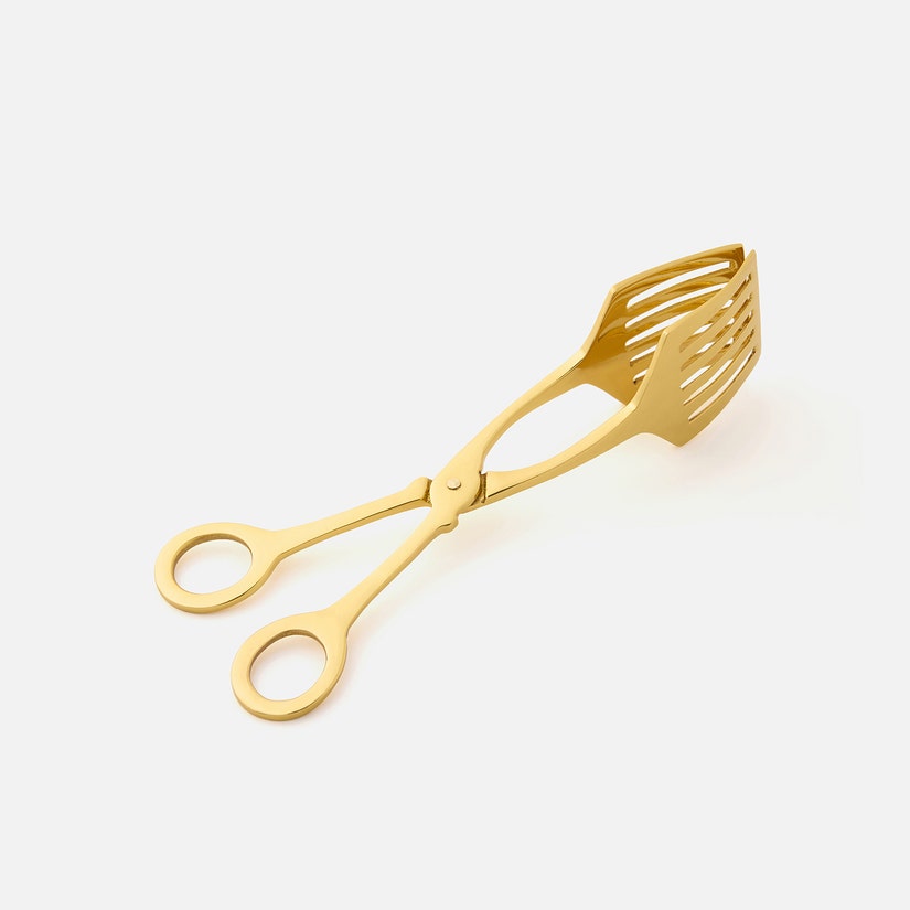 The Zena Serving Tongs by Blue Pheasant are gold-colored brass utensils with slotted, scoop-like ends and finger loops, designed for serving food. They are elegantly displayed on a plain white background.