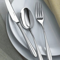 The Sambonet Dream Solid Handle Flatware 5 Piece Setting, featuring a knife, spoon, and fork, sits neatly on stacked white plates with light gray and yellow napkins placed nearby.