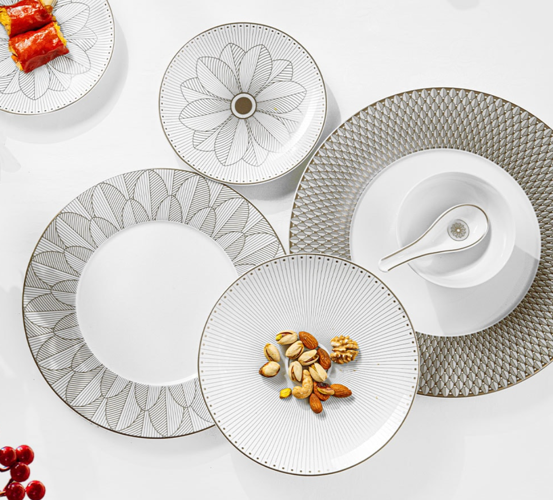 The Christofle Malmaison Imperiale Porcelain Dinnerware Platinum features decorative white plates with geometric and floral detailing, some serving nuts and sushi, arranged on a white surface with a porcelain soup spoon and red berries.
