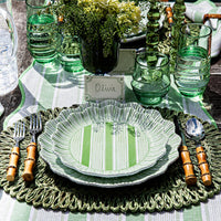 A table setting features Juliska’s Cabana Stripe Melamine Dinnerware Set of 4 - Seagrass, paired with bamboo-handled cutlery, green glassware, flowers, and an “Olivia” place card. These shatterproof dinner plates are dishwasher safe.