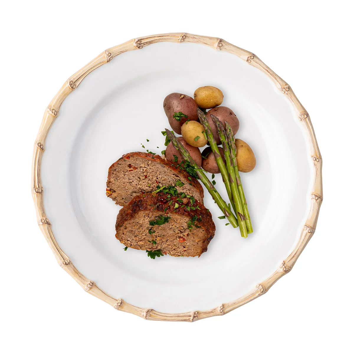 Two slices of meatloaf garnished with fresh herbs, accompanied by asparagus spears and a medley of small potatoes, beautifully presented on Juliska’s Bamboo Dinnerware for an elegant touch.