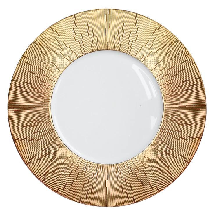 The Infini Prestige Gold Dinnerware by Haviland features a striking sunburst pattern around a white center, inspired by hand-painted Limoges porcelain.