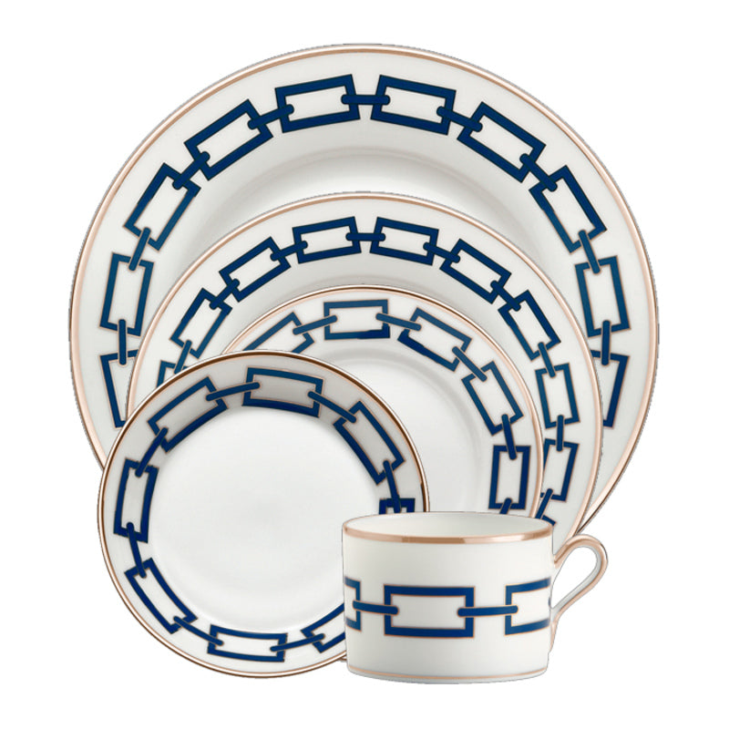 The Ginori 1735 Catene Zaffiro Dinnerware is a five-piece porcelain set with blue chain patterns and gold rims, including a dinner plate, salad plate, bread plate, saucer, and an elegant handled teacup.