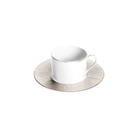 A Haviland Infini Prestige Platinum porcelain cup with handle rests on a round, textured silver saucer against a light gray background.