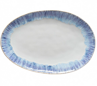 The Costa Nova Brisa Blue Dinnerware oval ceramic plate features a white center and a blue textured rim. Expertly crafted in Portugal, this stoneware piece is shown on a white background.