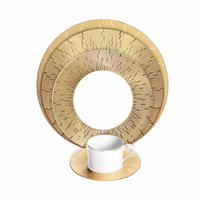 A white teacup with a gold handle rests on a gold saucer, in front of Haviland Infini Prestige Gold Dinnerware, featuring hand-painted Limoges porcelain plates with concentric circular designs and fine lines.