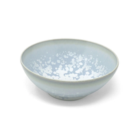The Song Ocean Dinnerware by Jaune De Chrome is a round, shallow ceramic bowl inspired by French style, with a pale blue glaze and white speckles inside, displayed on a plain white background.