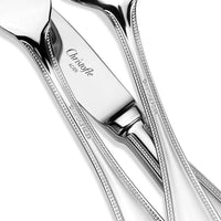 A close-up of the Perles 5 Piece Setting by Christofle shows polished stainless steel flatware with beaded edges; knives and spoons overlap, displaying the engraved brand name on each elegant handle.