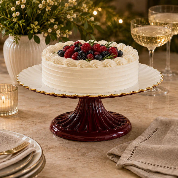 A round cake topped with berries on an Encanto Vienna Pedestal Cake Plate - Bordeaux & White, featuring a handcrafted aluminum top and a deep red pedestal base.