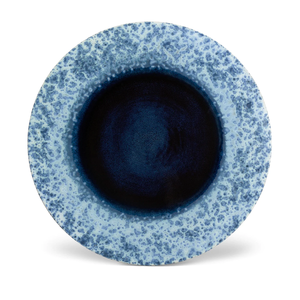 The L'Objet Terra Platter Charger Indigo features a round ceramic design with a dark blue center and lighter speckled rim, finished in glossy elegance. Perfect for refined settings, it's shown on a white background.