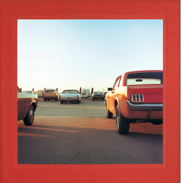 A vibrant sunset photo of vintage cars parked in an open lot, with a clear sky backdrop and red border, evokes the style of William Eggleston: 2 1/4 by ARTBOOK DAP/INGRAM.