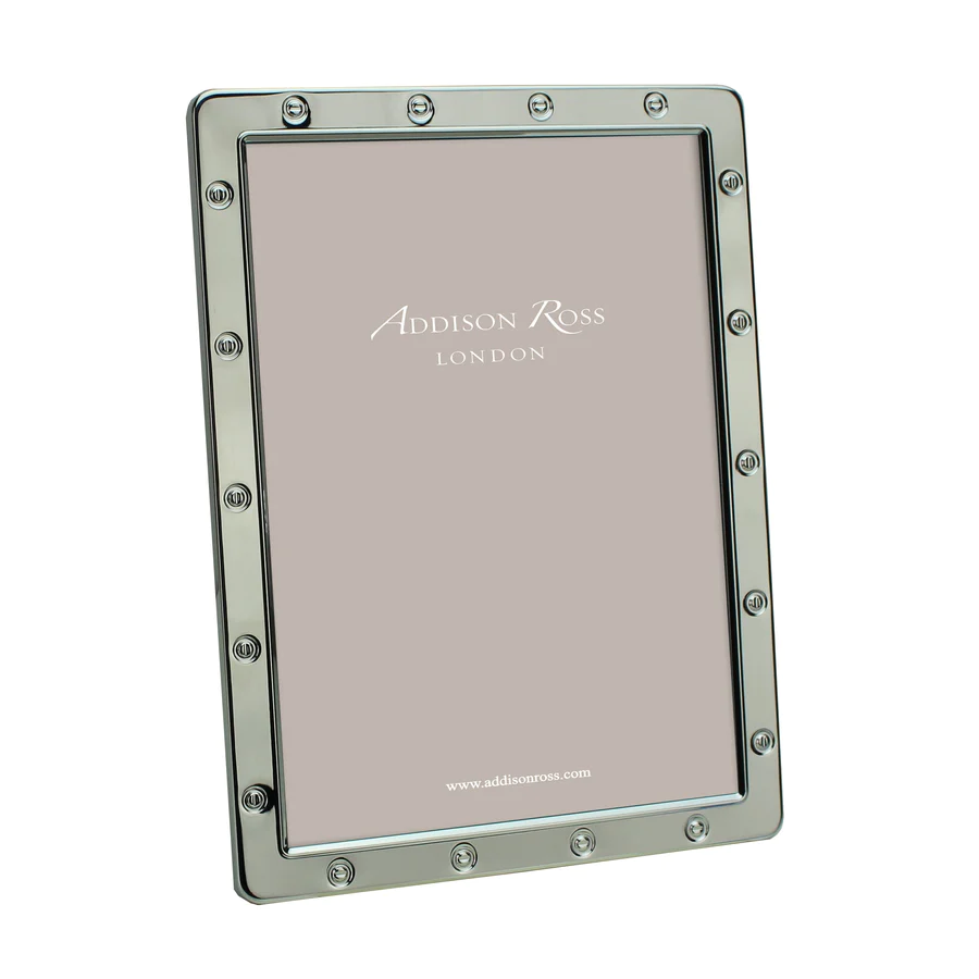 The Addison Ross Locket Frame Silver features a stylish rivet-style border, stands upright with a blank insert and velvet backstand, and is elegantly presented in a gift box.