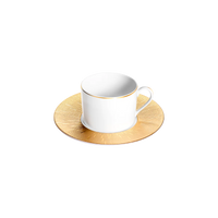 A white Haviland Infini Prestige Gold teacup with a gold rim rests on a fully gold, textured saucer, both crafted from Limoges porcelain. A plain light gray background accentuates the elegance of this dinnerware piece.