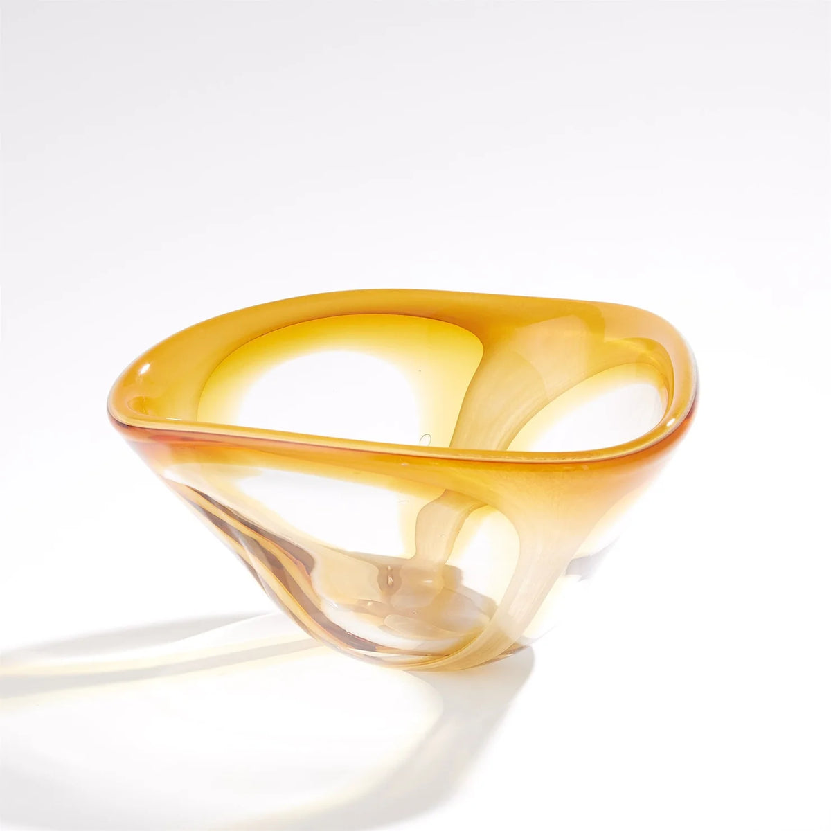 The Enigma Bowl - Amber by Global Views / Surya is a handblown art glass piece featuring a transparent amber hue, smooth curved edges, and an organic asymmetrical shape. Set against a plain white background, this bowl functions as both a striking decorative catchall and an elegant accent for any space.