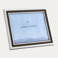 The Georg Jensen Manhattan Picture Frame is a square silver stainless steel frame with a dark inner border, featuring a placeholder card reading "Georg Jensen" and "By appointment to Her Majesty the Queen of Denmark" above a mountain graphic.