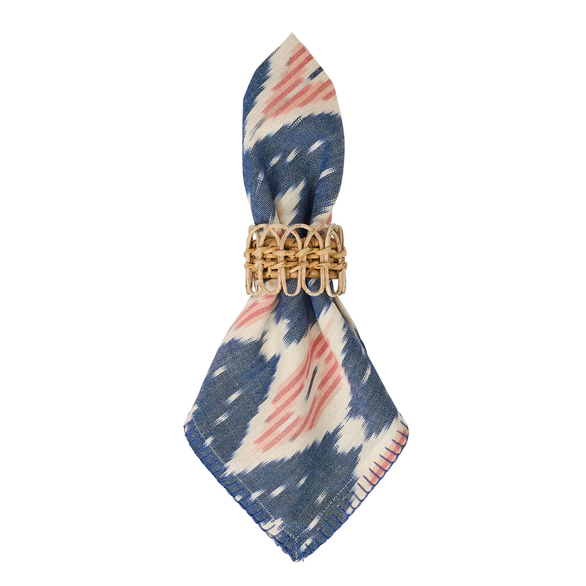 The Juliska Ikat Napkin - Set/4 features blue, white, and pink patterned cloth napkins, elegantly folded and held upright by a tan woven rattan ring—an ideal touch for relaxed island living.