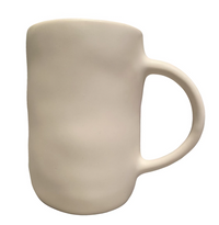 The Urban Dinnerware Matte White mug by Alex Marshall Studios features a plain, unglazed ceramic finish with a rounded, slightly uneven shape and large curved handle, evoking handmade stoneware. Shown against a white background.