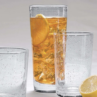 Three Bellini Glassware pieces by Mariposa, two empty and one filled with iced tea and lemon slices, sit on a light surface. A lemon wedge rests nearby, while water droplets glisten on these stylish, dishwasher safe glasses.
