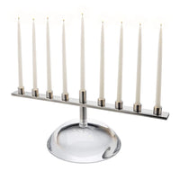 A nature-inspired Riverstone Simon Pearce Menorah made of glass with a linear metal candle holder holding nine lit white taper candles.