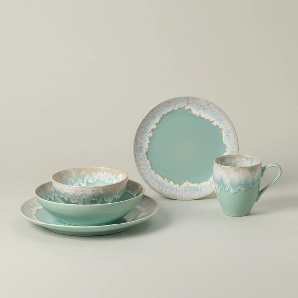 Taormina Aqua Dinnerware set in aqua ceramic, including a dinner plate, a shallow bowl, a smaller bowl, and a mug, all featuring an irregular, textured white and brown rim.