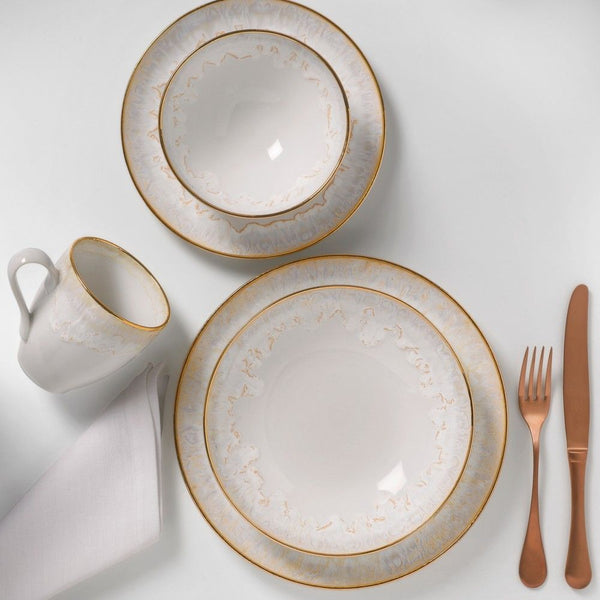 The Taormina Dinnerware White & Gold by Casafina/Costa Nova features gold-rimmed stoneware plates, a hand-painted 18-karat gold-rimmed bowl, a matching mug, white napkin, and rose gold flatware—made in Portugal.