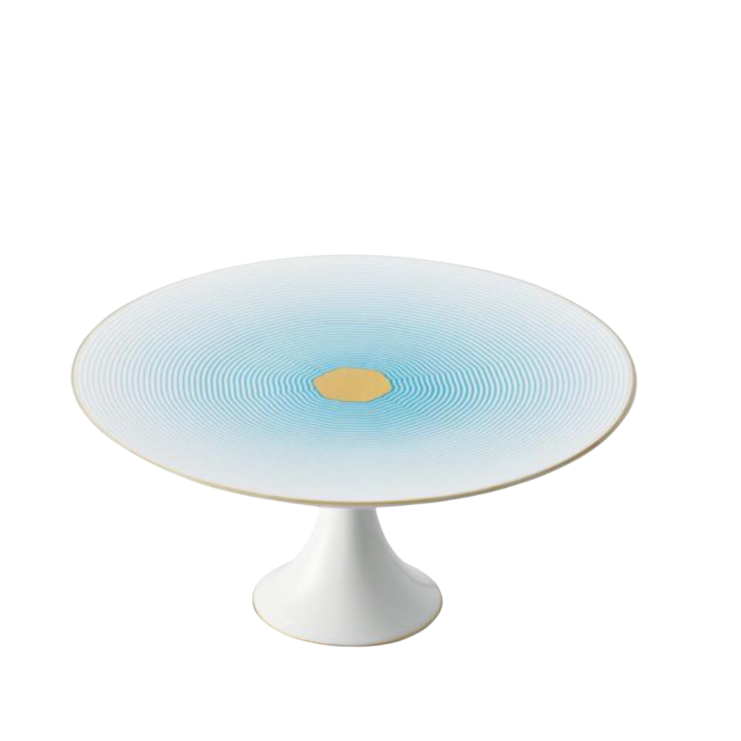 The Aura Dinnerware cake stand by Raynaud is a white porcelain piece, made in France, with blue concentric circles and a gold center on its wide round top, set on a short pedestal base.