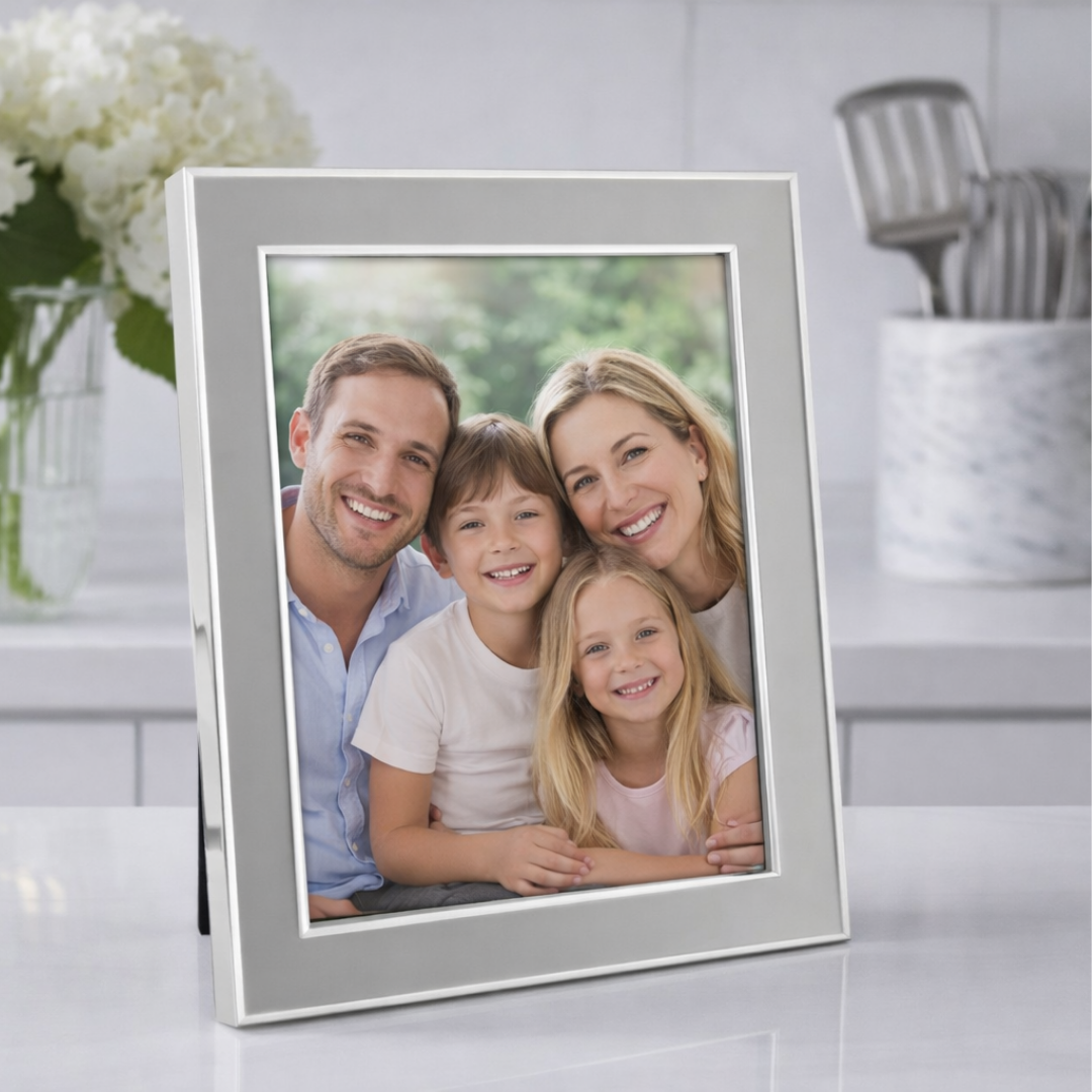 A framed family photo rests on the kitchen counter in an Addison Ross Enamel Thin Chiffon Silver Frame, showing a smiling man, woman, boy, and girl together with greenery softly blurred behind them.