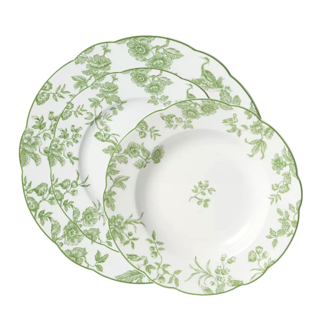 Three Albertine Dinnerware plates by Bernardaud, white ceramic with scalloped edges and green floral designs, are displayed fan-like—a graceful, poetic accent inspired by classic Bernardaud style.