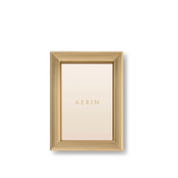 The Alessio Frame by Aerin is a gold rectangular desk frame with a reeded design and a cream placeholder showing "AERIN" in gold lettering on a plain white background.