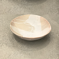 The Round Ceramic Bowls - Stone by Alex Marshall Studios feature a matte beige glaze with abstract white patterns, beautifully highlighting handmade craftsmanship as they rest on a speckled light-grey surface.