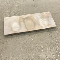 The Three Part Stone Rectangle Platter by Alex Marshall Studios is a handmade ceramic piece with smooth, wavy indentations and a pale marbled beige finish, shown resting on a speckled concrete floor.