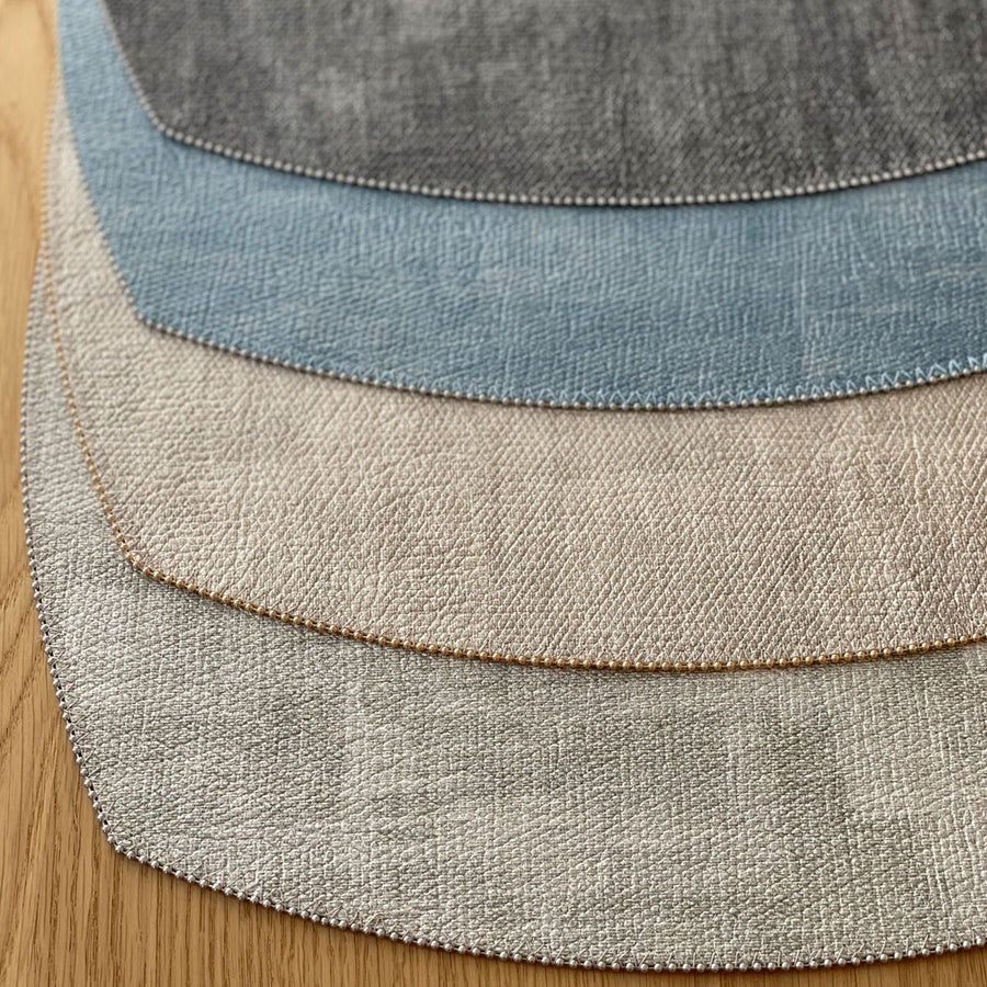 Four textured fabric swatches in gray, beige, light blue, and dark gray are fanned out on wood, echoing the elegant design of Bodrum’s Allure Elliptic Square Placemat Set of 4.