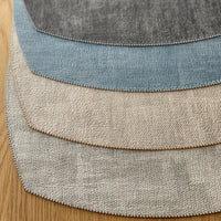 Four textured fabric swatches in gray, beige, light blue, and dark gray are fanned out on wood, echoing the elegant design of Bodrum’s Allure Elliptic Square Placemat Set of 4.