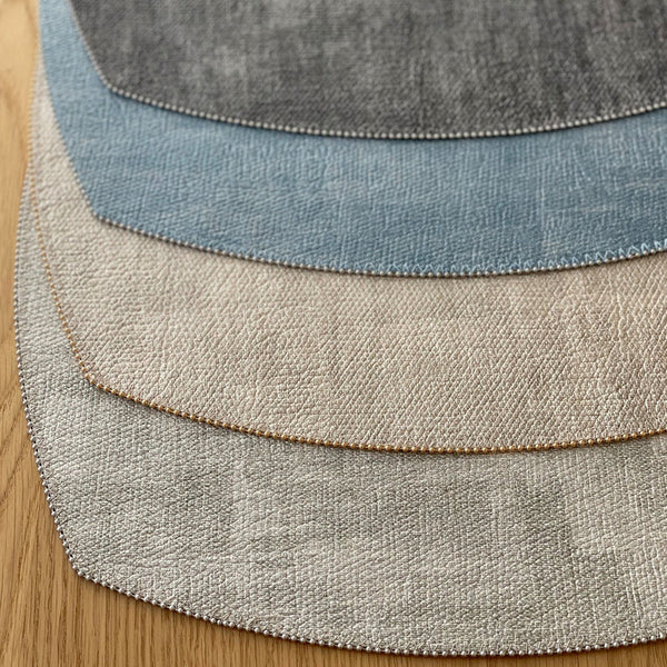 Four textured fabric swatches in gray, beige, light blue, and dark gray are fanned out on wood, echoing the elegant design of Bodrum’s Allure Elliptic Square Placemat Set of 4.